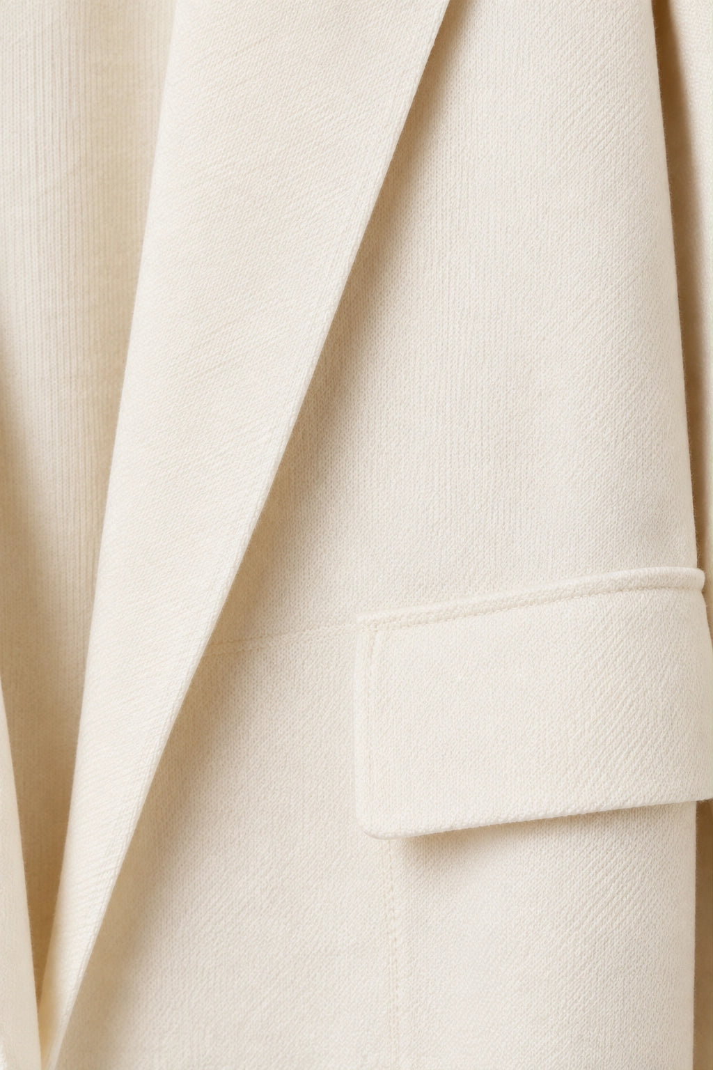 Close-up of a cream-colored textured blazer fabric, showing the lapel and a matching welt pocket.
