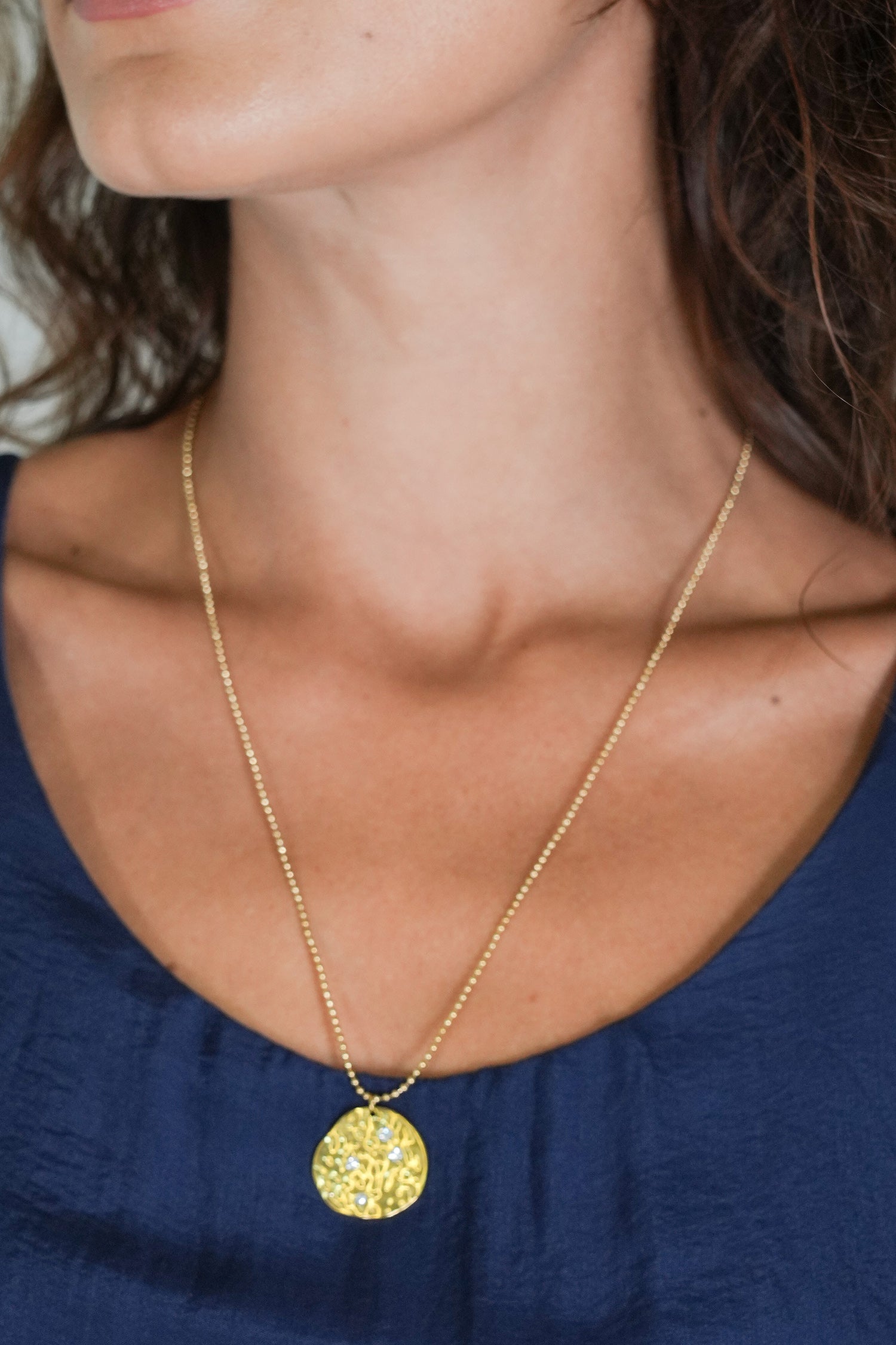 Gold necklace with a pendant worn by a person against a blue top.