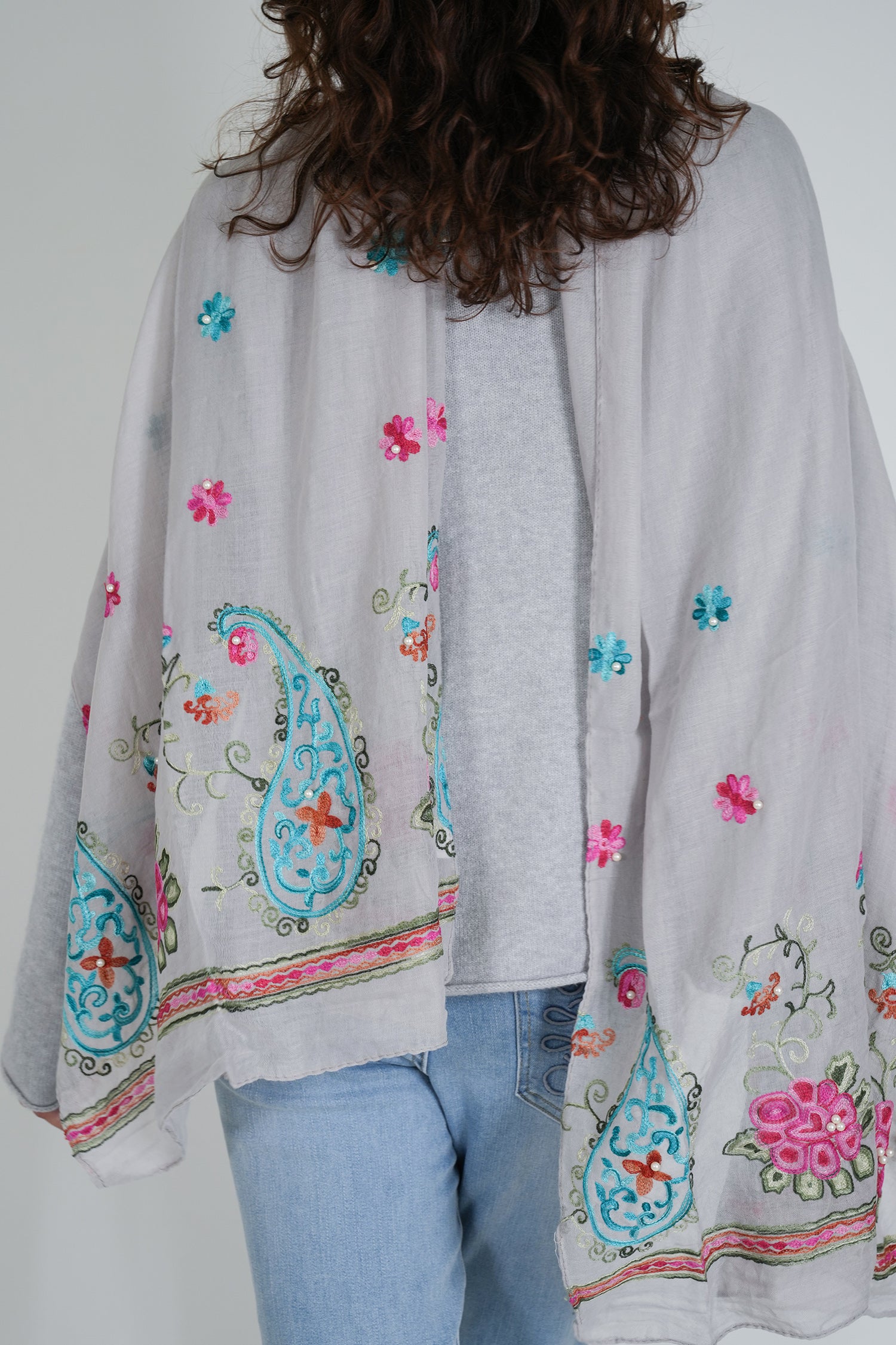 Person wearing a light gray cardigan with colorful floral and paisley patterns on a plain background