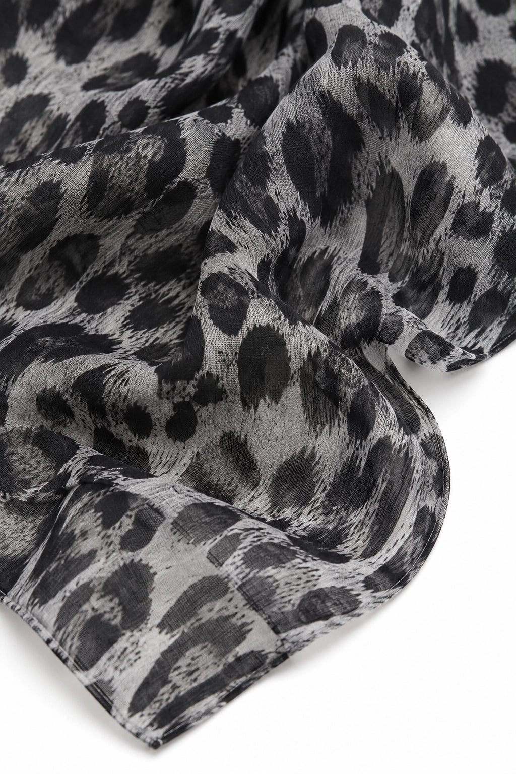 A close-up of a lightweight scarf with a black and gray leopard print pattern, draped elegantly against a clean white background.