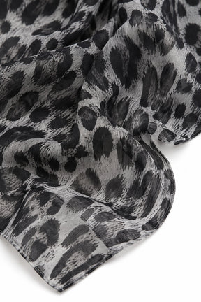 A close-up of a lightweight scarf with a black and gray leopard print pattern, draped elegantly against a clean white background.