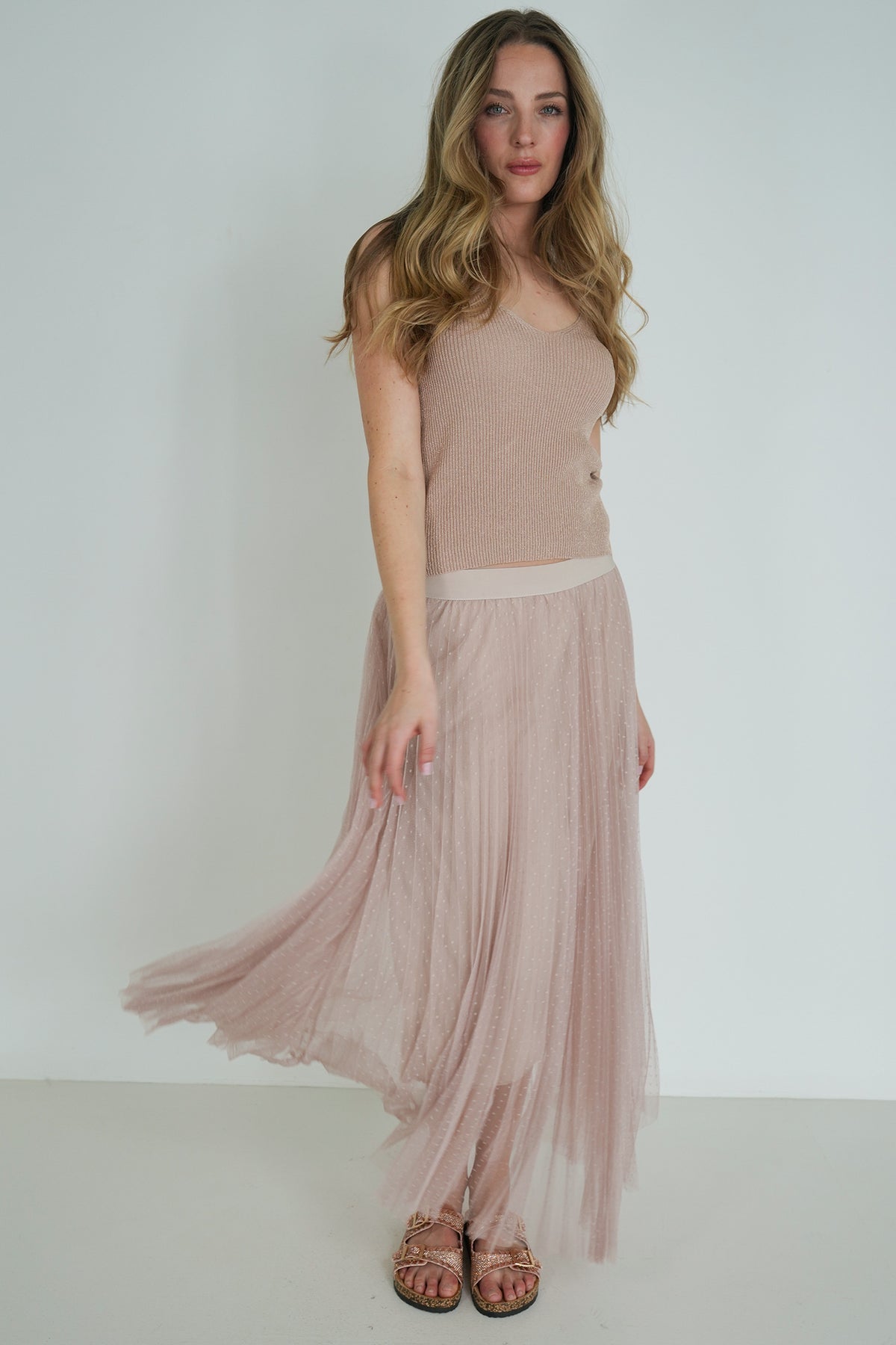 Model walking in beige ribbed sleeveless top and blush pink pleated tulle skirt, showing movement and flow.