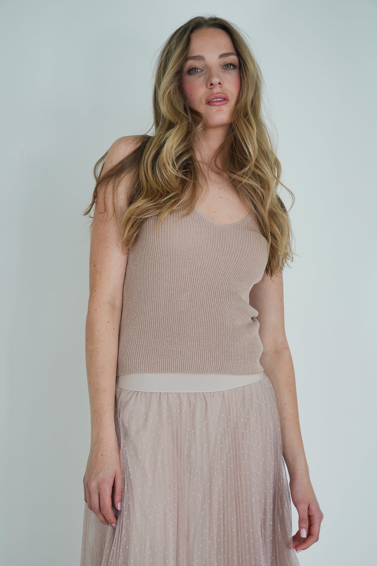 Model wearing a beige ribbed sleeveless top paired with a blush pink pleated tulle midi skirt, posing indoors.