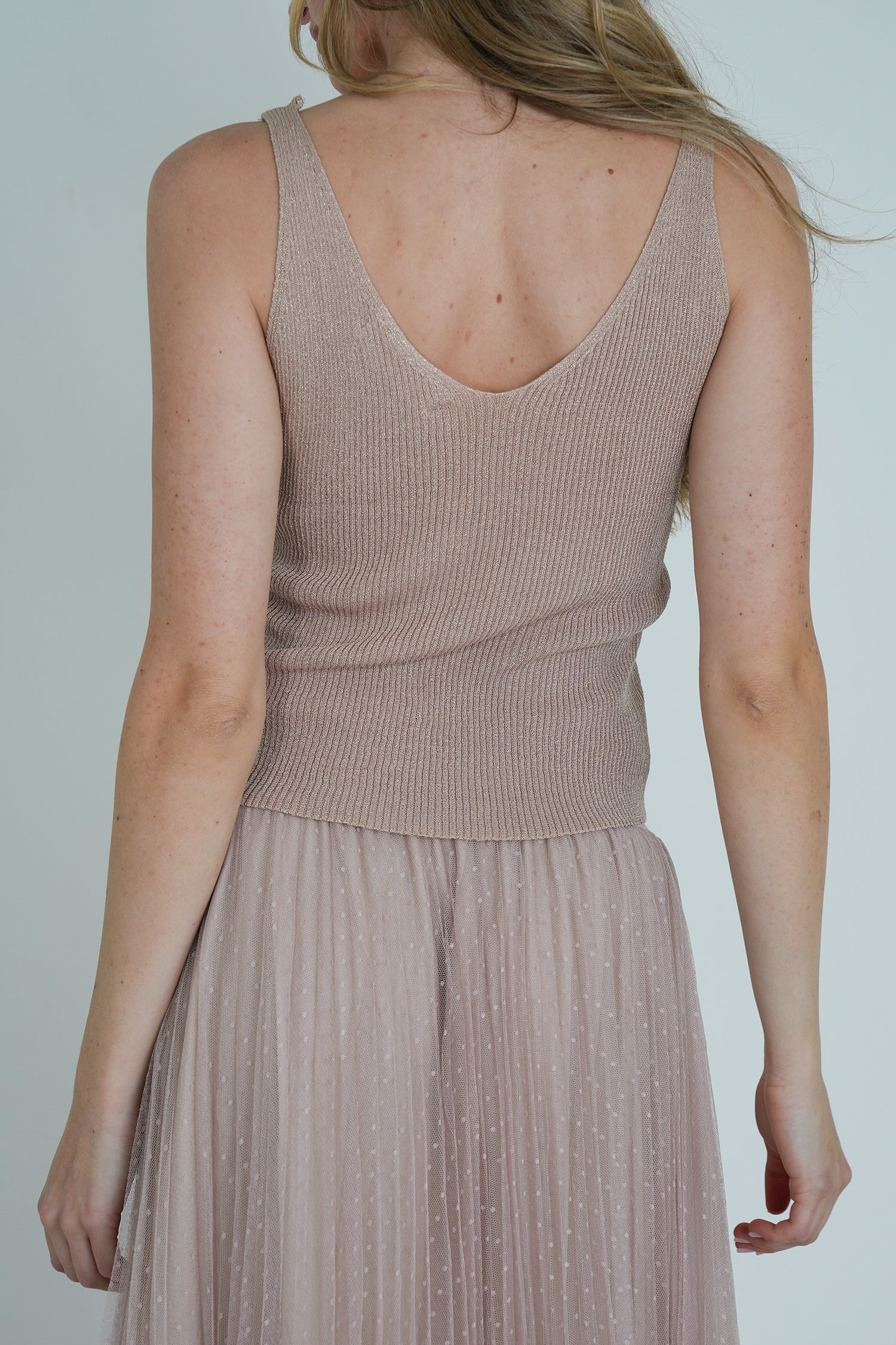 Back view of model wearing beige ribbed V-neck top and blush pink pleated tulle midi skirt, showing texture and fit.