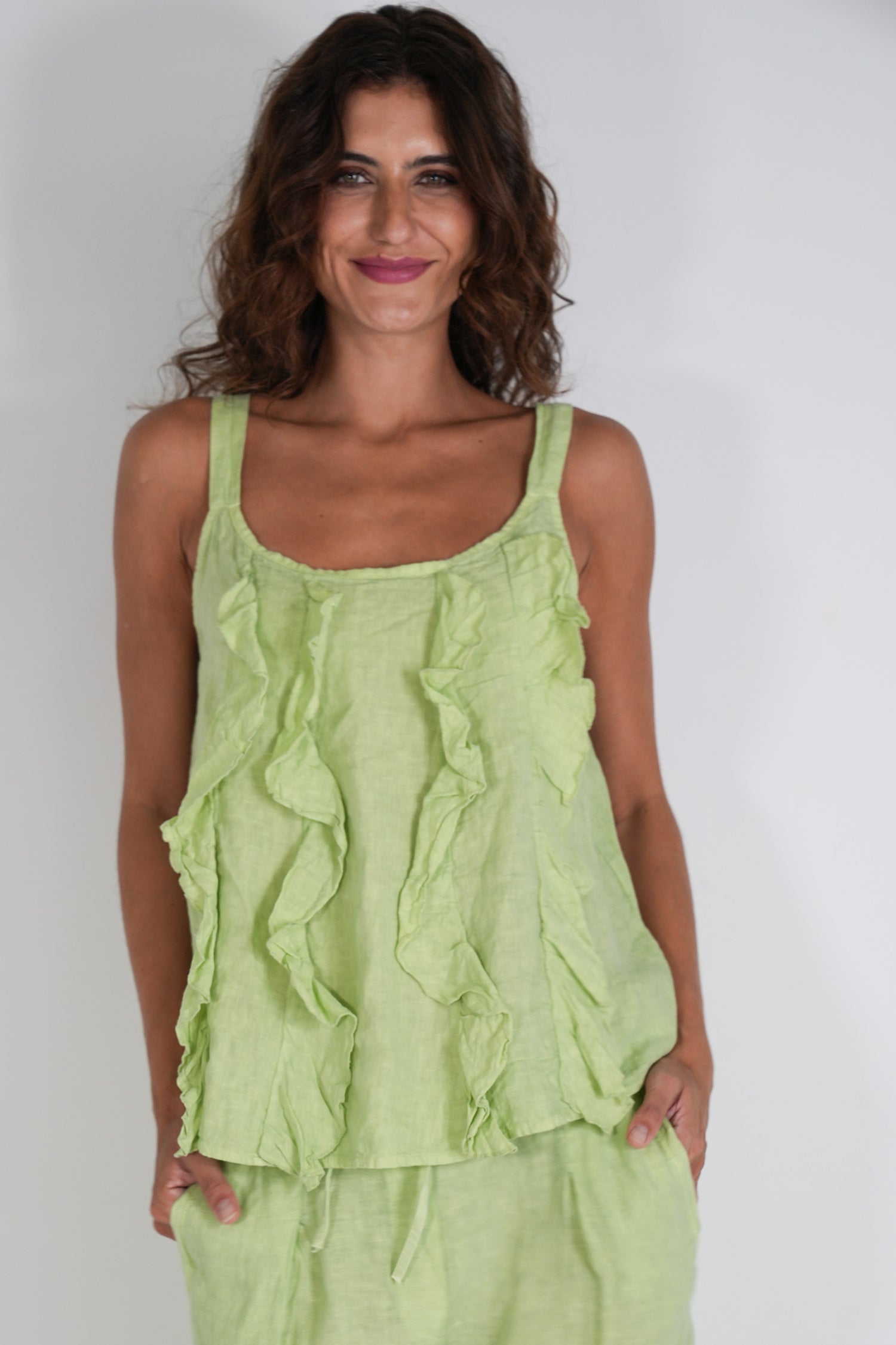 Woman wearing a light green ruffled top and pants on a white background