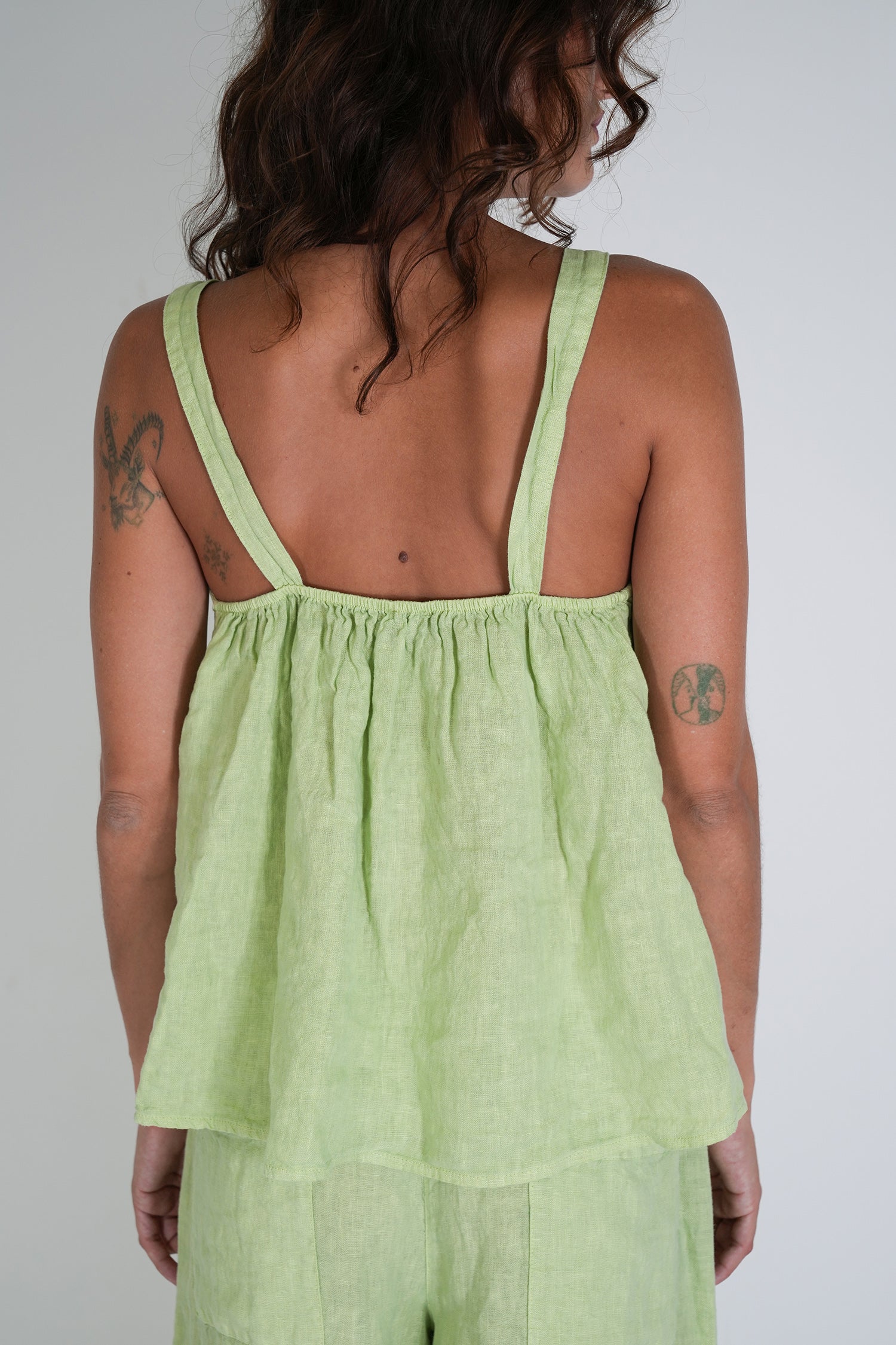Woman wearing a light green sleeveless top with thin straps on a plain background