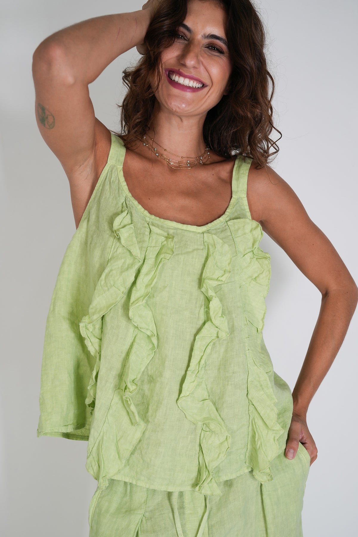 Woman wearing a light green sleeveless top and pants against a plain background