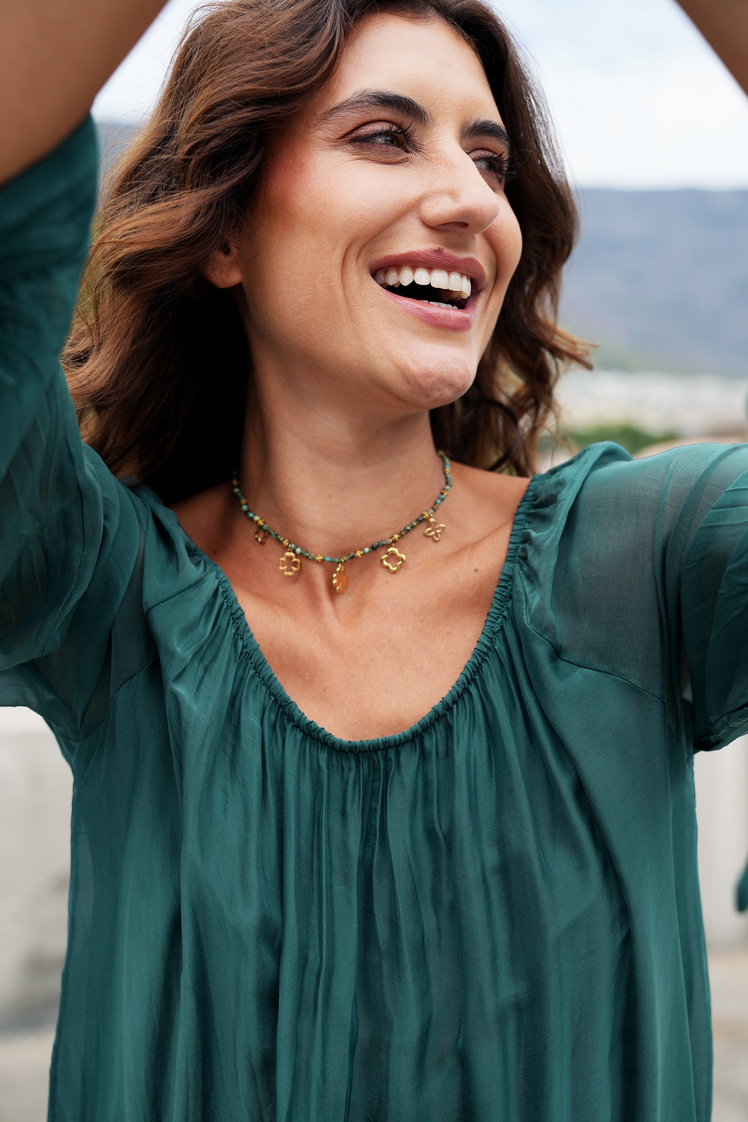 Woman wearing a green blouse with a necklace, standing outdoors.