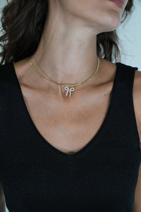 Close-up of a person wearing a gold necklace with a small pendant against a neutral background