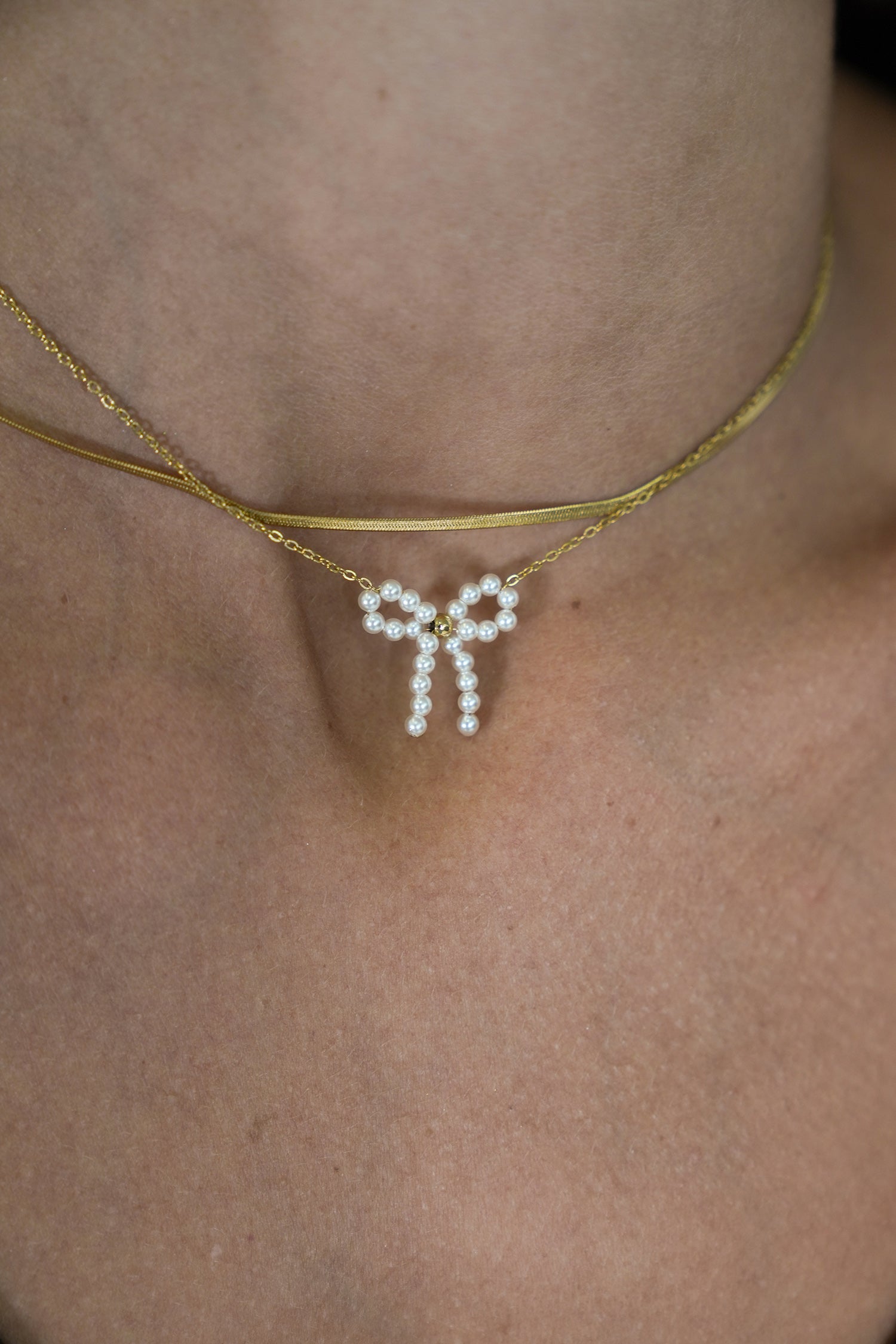 Pearl bow pendant necklace on gold chain, close-up on neck