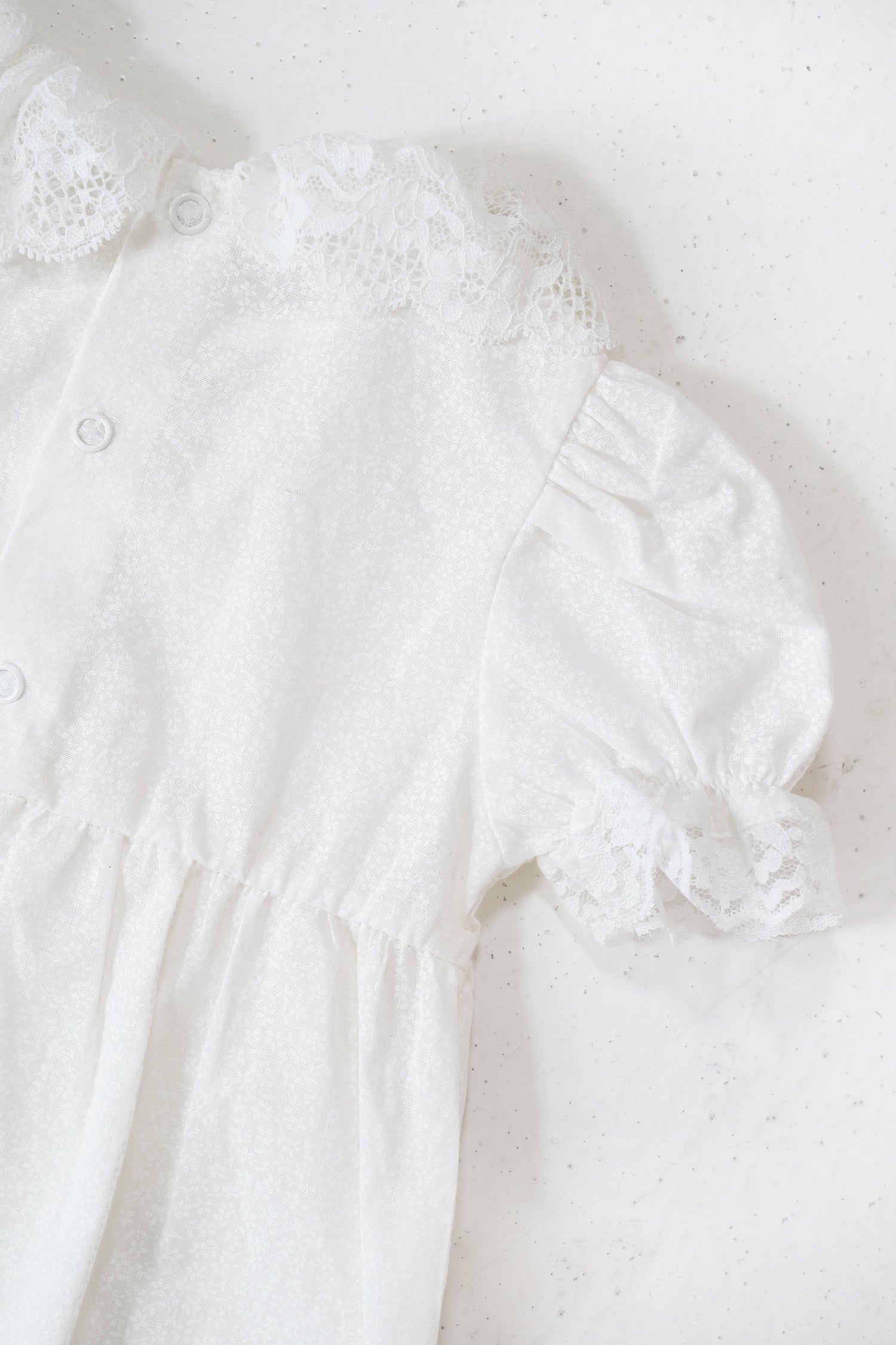 White baby outfit with lace details on a light background