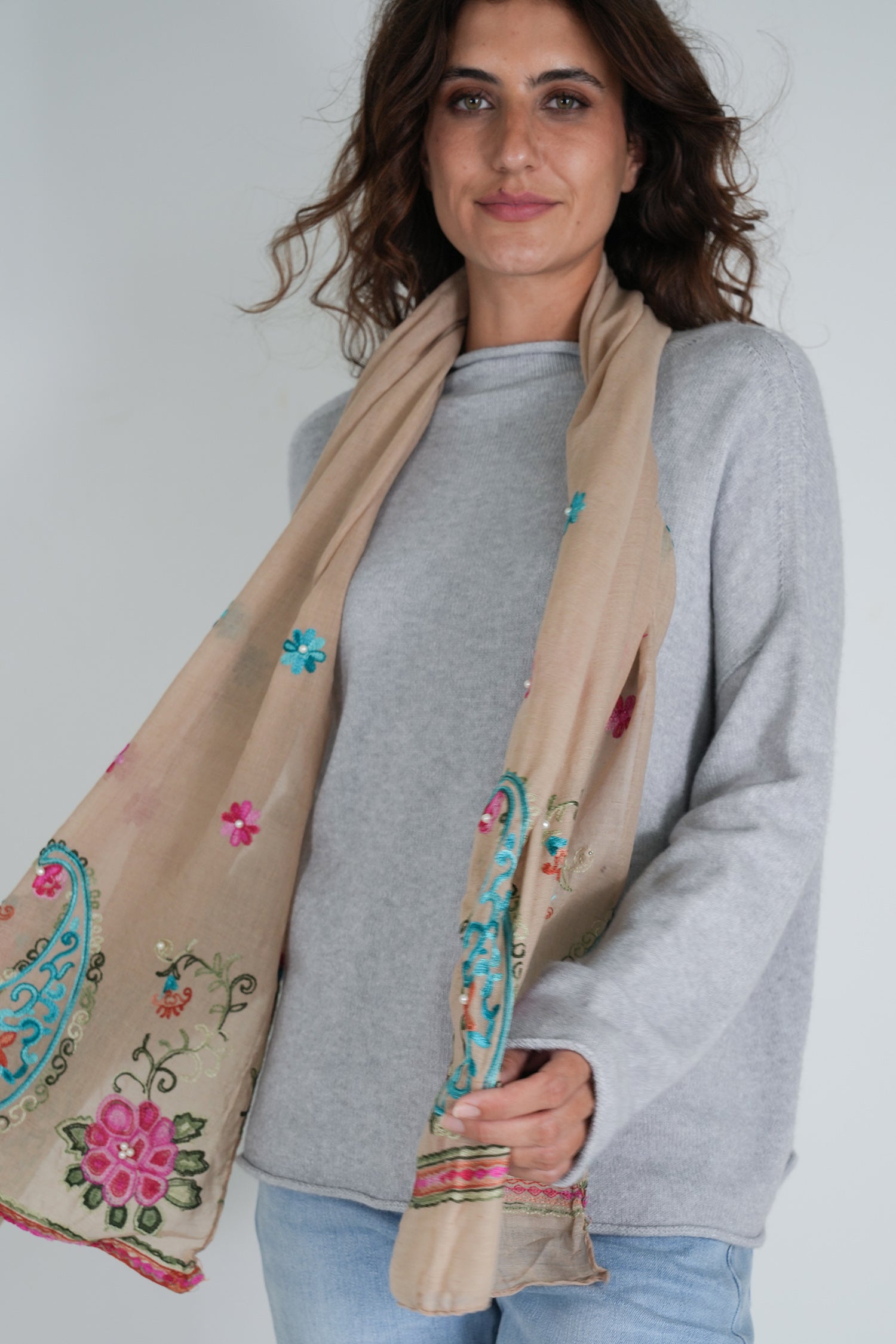 Woman wearing a beige scarf with floral embroidery against a white background