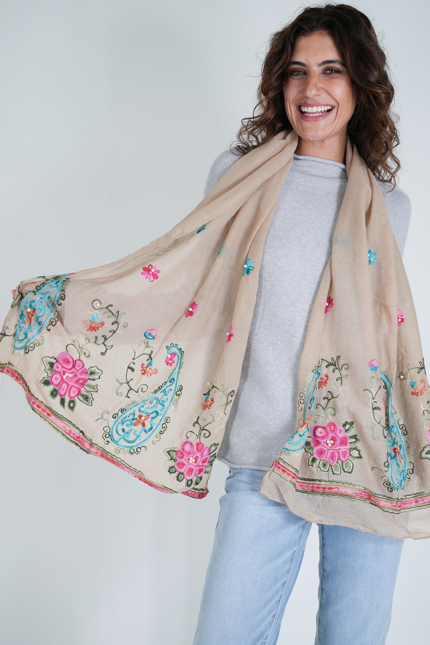 Woman wearing a beige scarf with floral and paisley patterns on a plain background