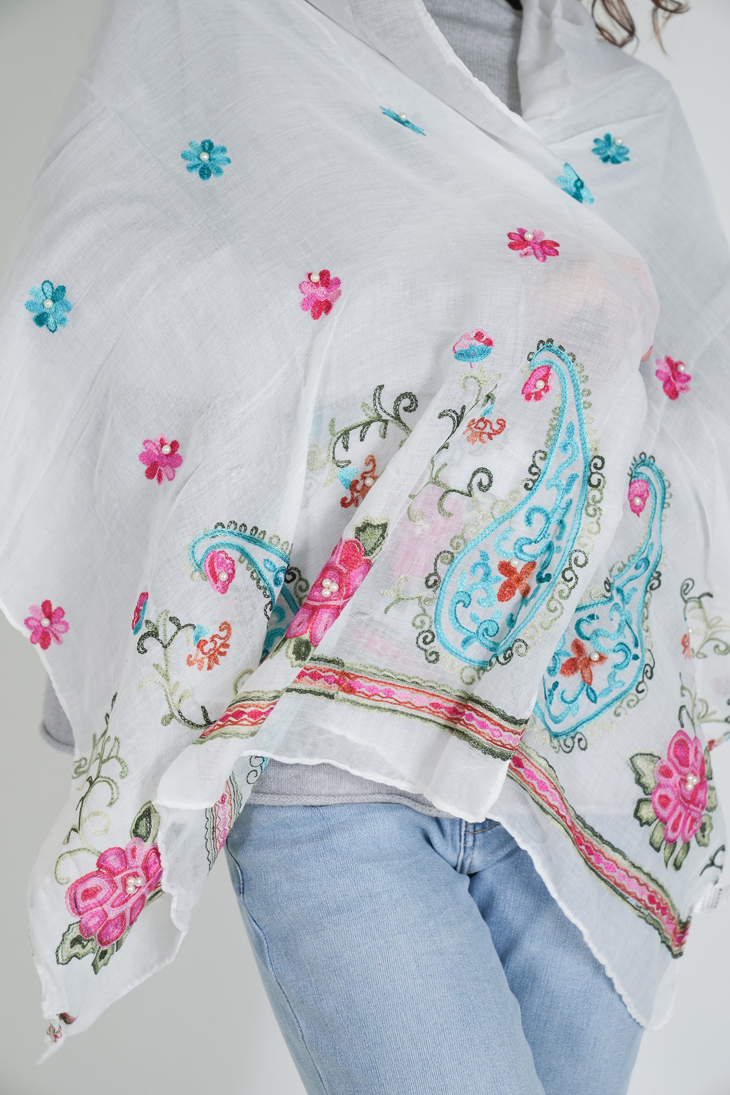White scarf with colorful floral and paisley patterns draped over a person wearing light blue jeans.