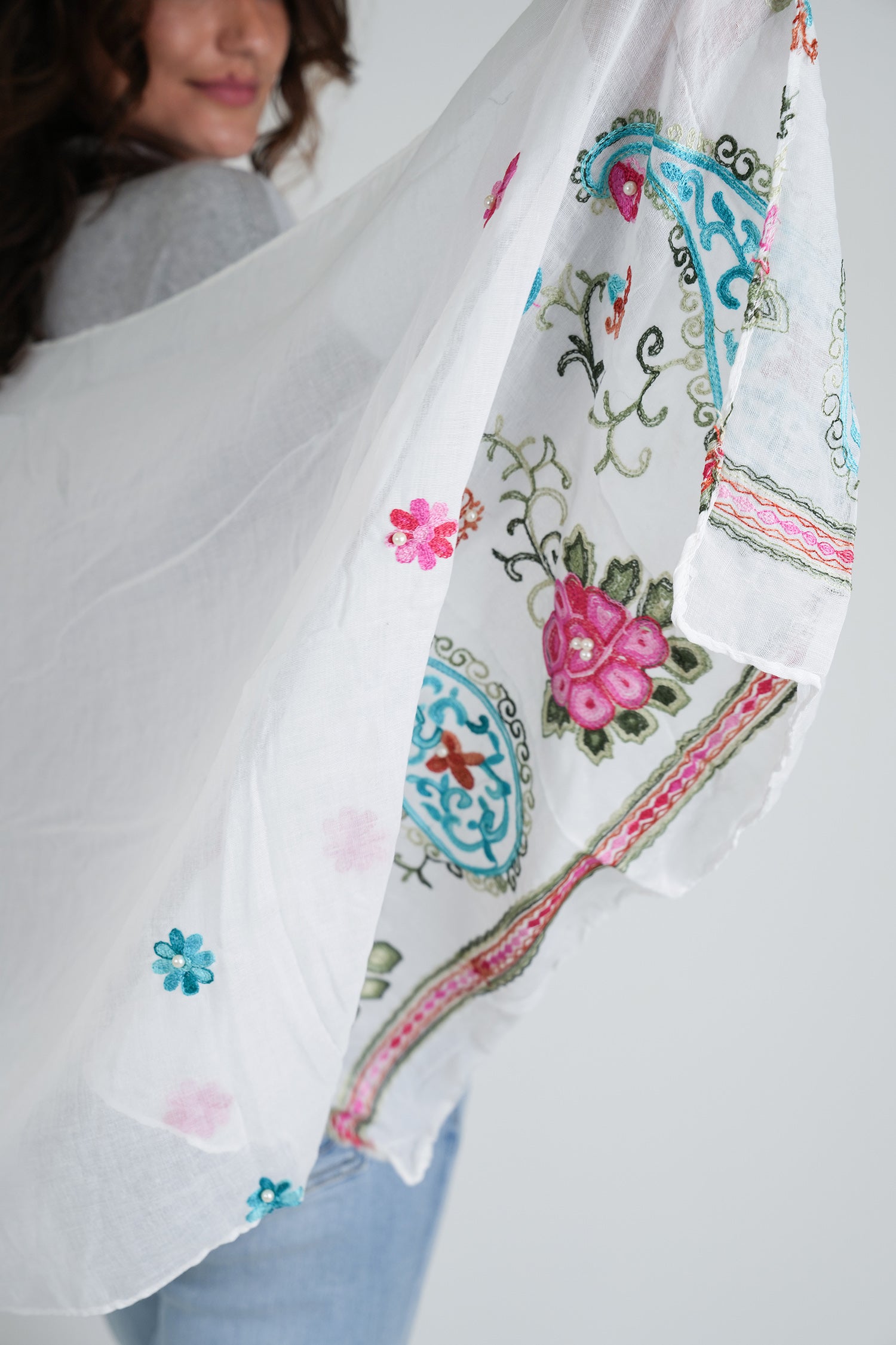 Woman holding a white scarf with colorful floral and geometric embroidery.