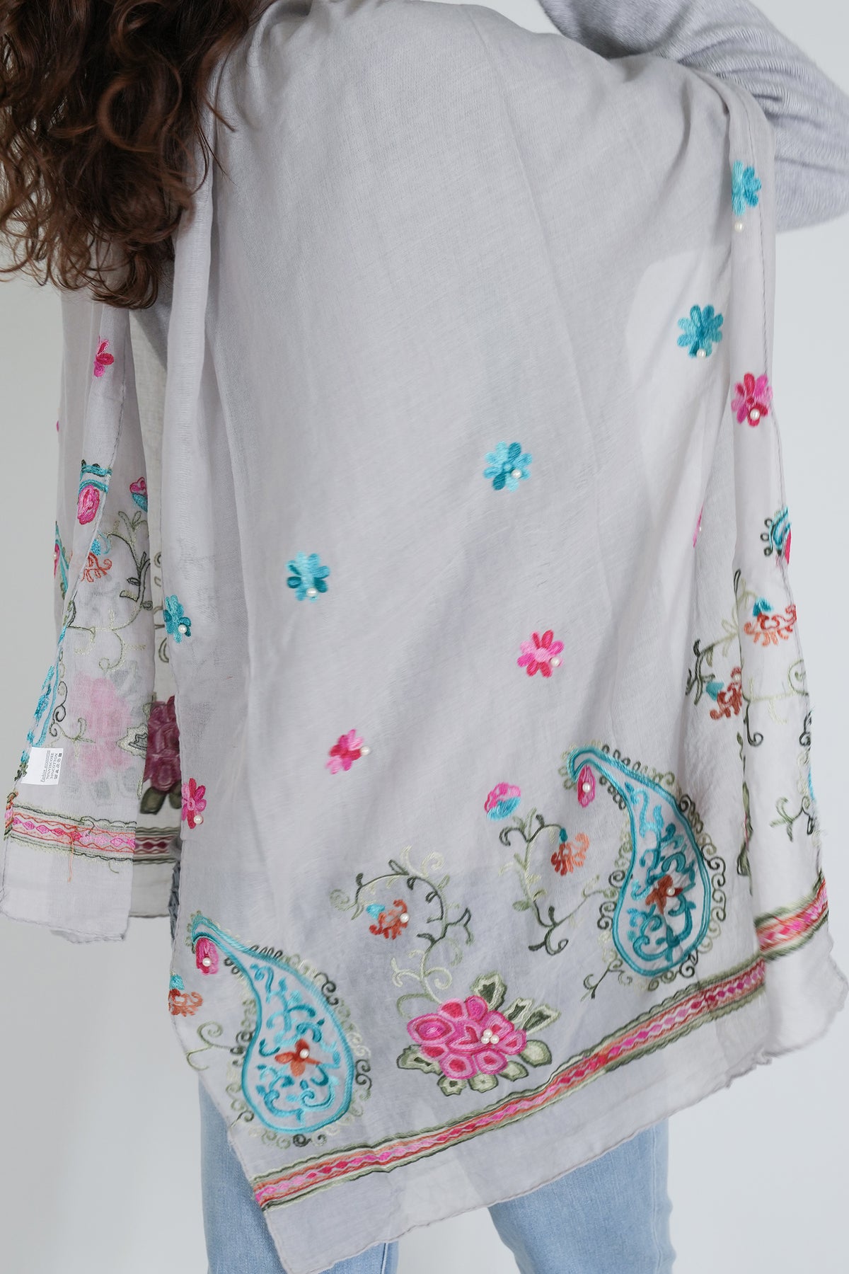 Light gray scarf with colorful floral and paisley patterns held by a person.