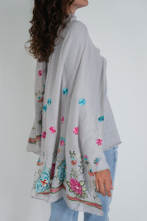 Woman wearing a light gray kimono-style garment with colorful floral embroidery on a plain background