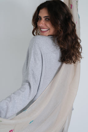 Woman wearing a gray sweater and beige scarf against a white wall
