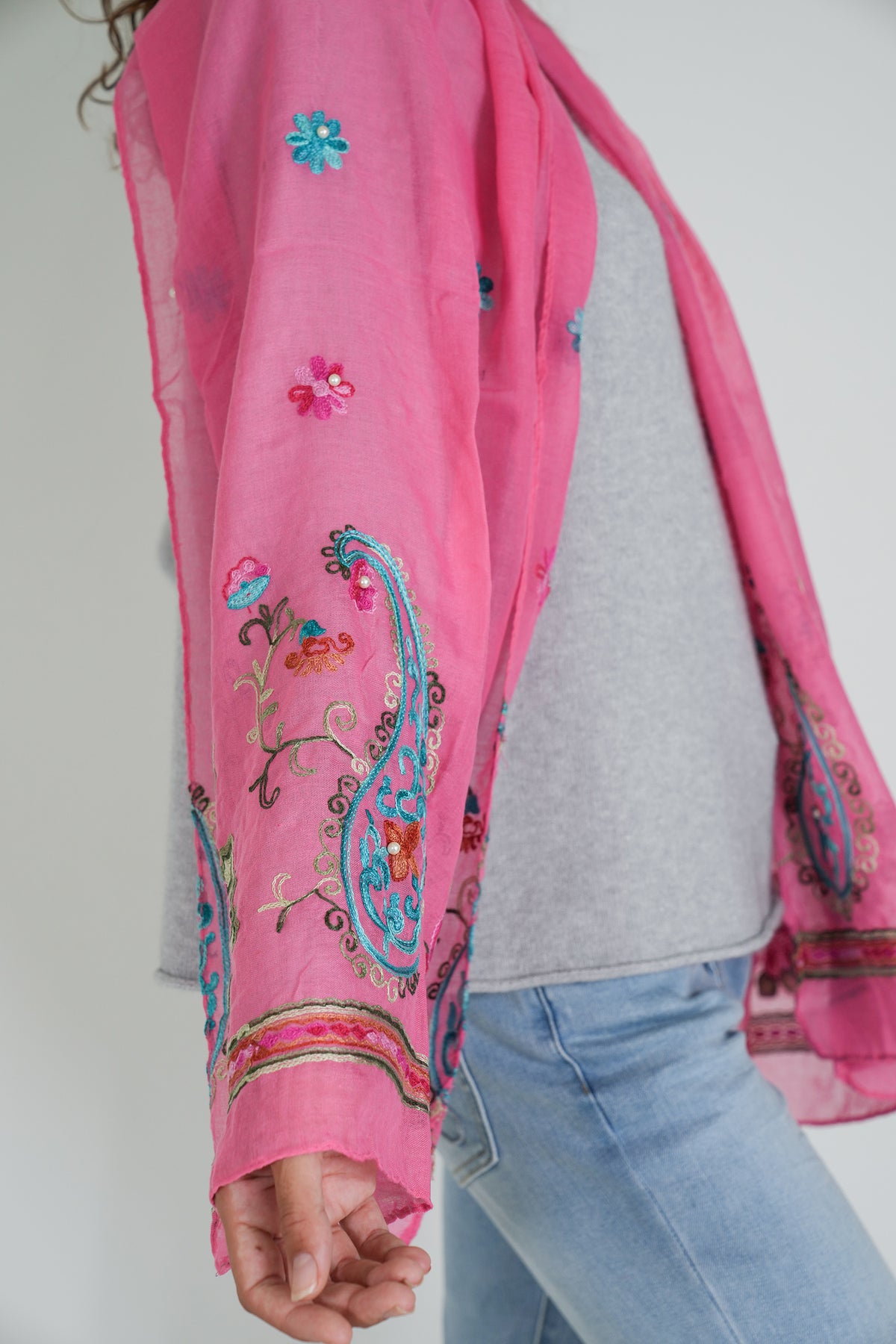Person wearing a pink embroidered scarf with a plain background