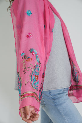 Person wearing a pink embroidered scarf with a plain background