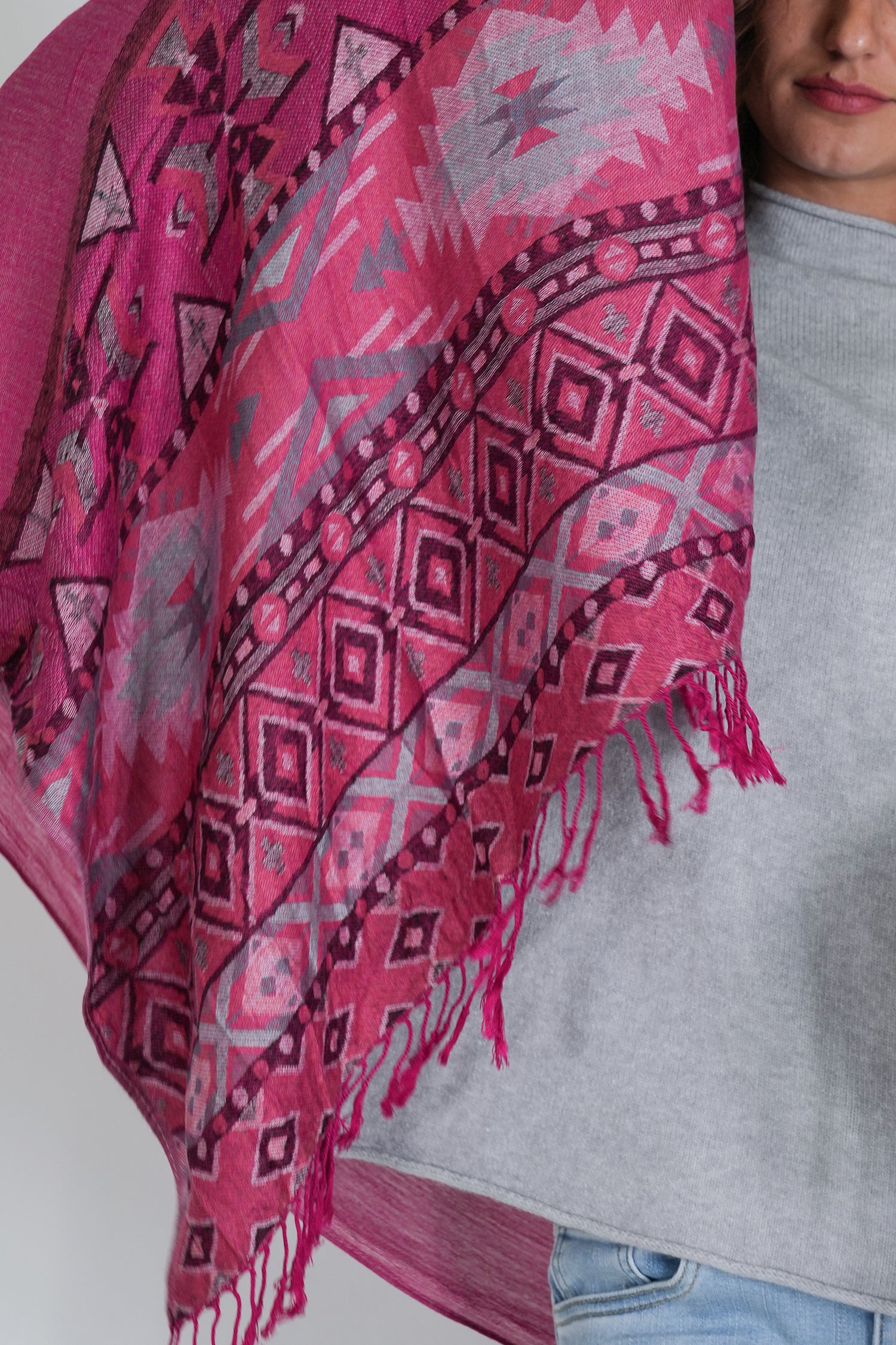 Person wearing a pink patterned scarf with a gray shirt and blue jeans.