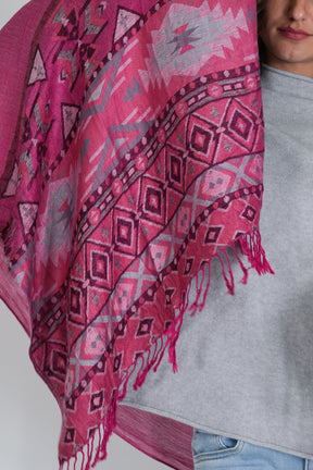 Person wearing a pink patterned scarf with a gray shirt and blue jeans.