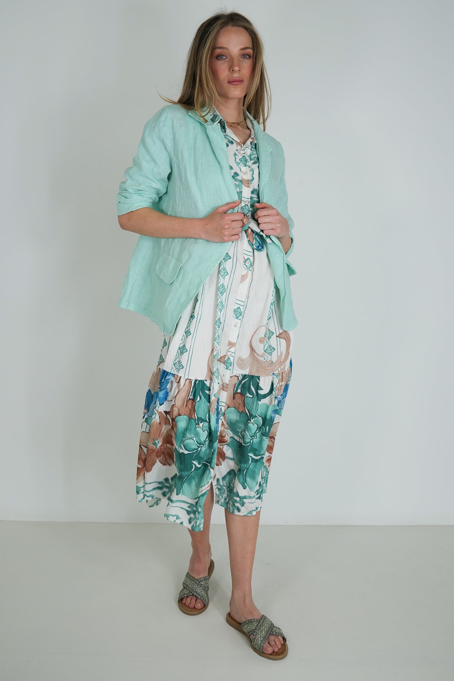 Woman wearing a light green jacket over a floral dress on a plain background