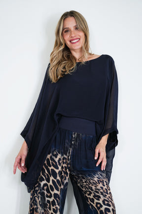 Woman wearing a navy blue top and leopard print pants against a white background