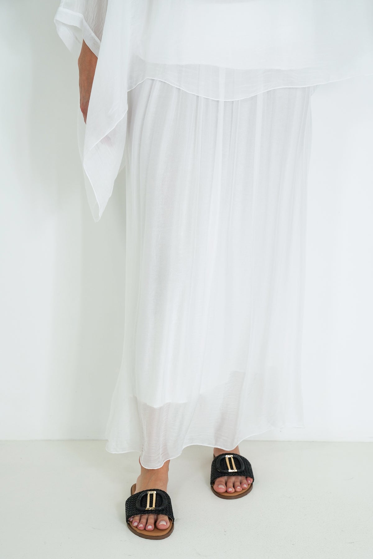 Person wearing a white outfit with black sandals on a white background