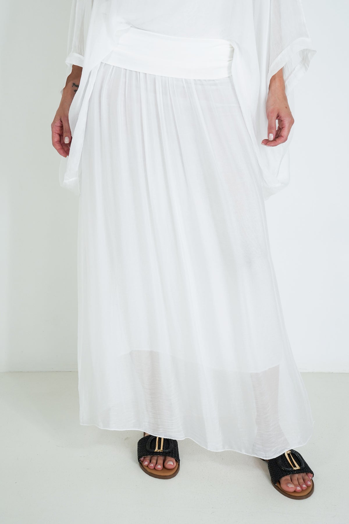 Person wearing a long white dress with black sandals on a white background