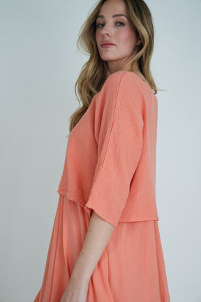 Side view of coral long-sleeve flowy midi dress with soft textured fabric, model posing against a plain backdrop.