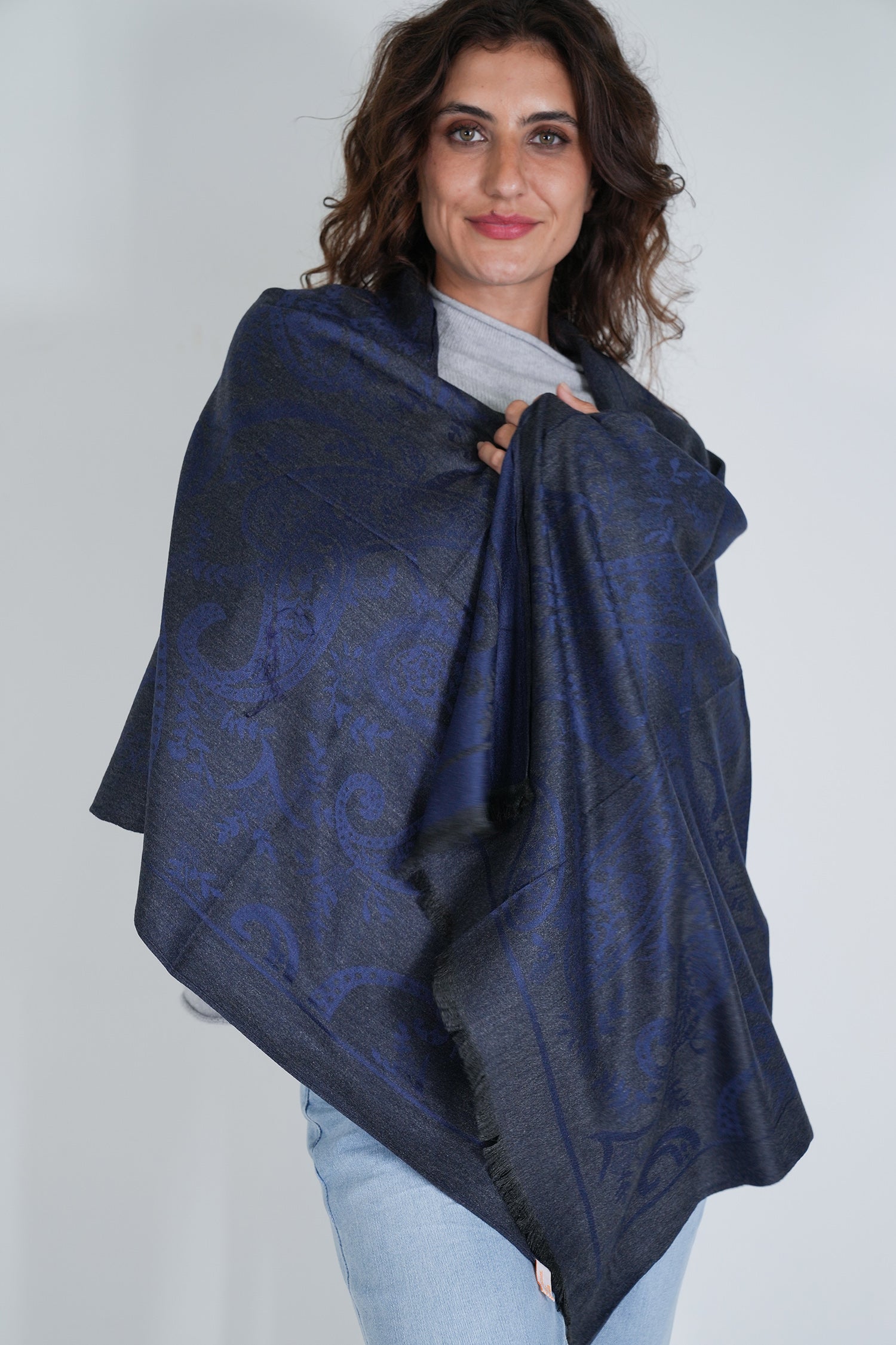 Woman wearing a dark blue patterned shawl over her shoulders against a plain background