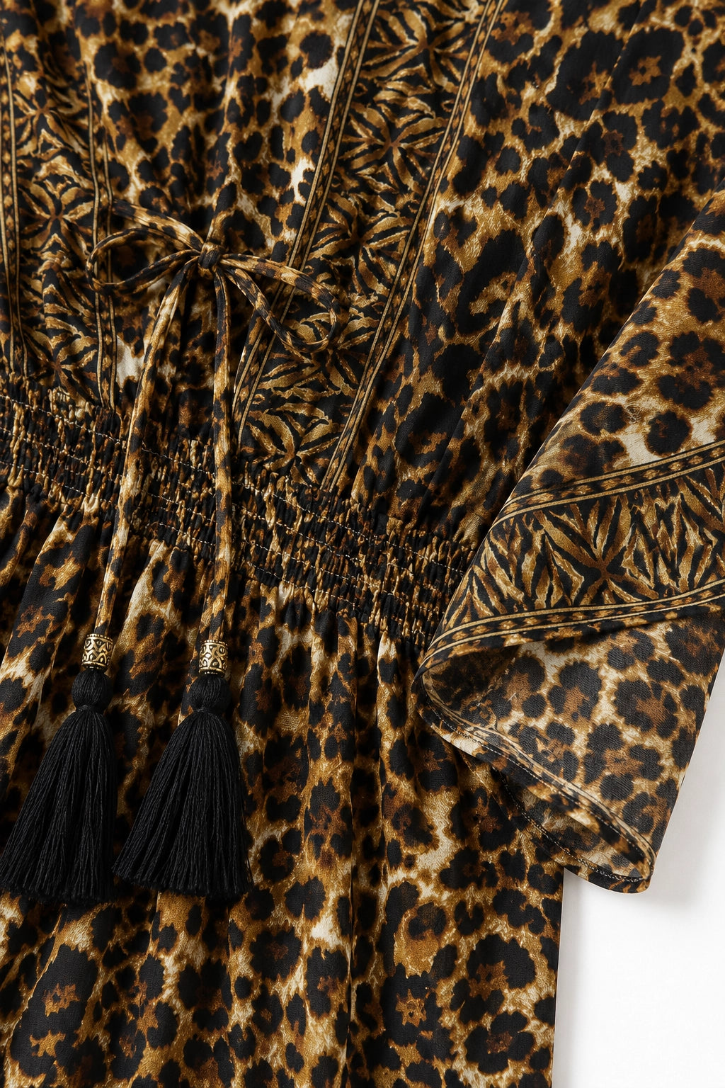 Close-up of a leopard-print garment with black tassels and a smocked waist, showing brown, black, and tan pattern details.