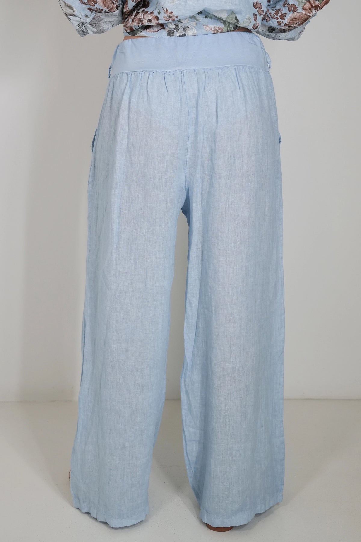 Light blue wide-leg linen pants shown from the back, worn by a model with a floral long-sleeve top partially visible at the top edge.