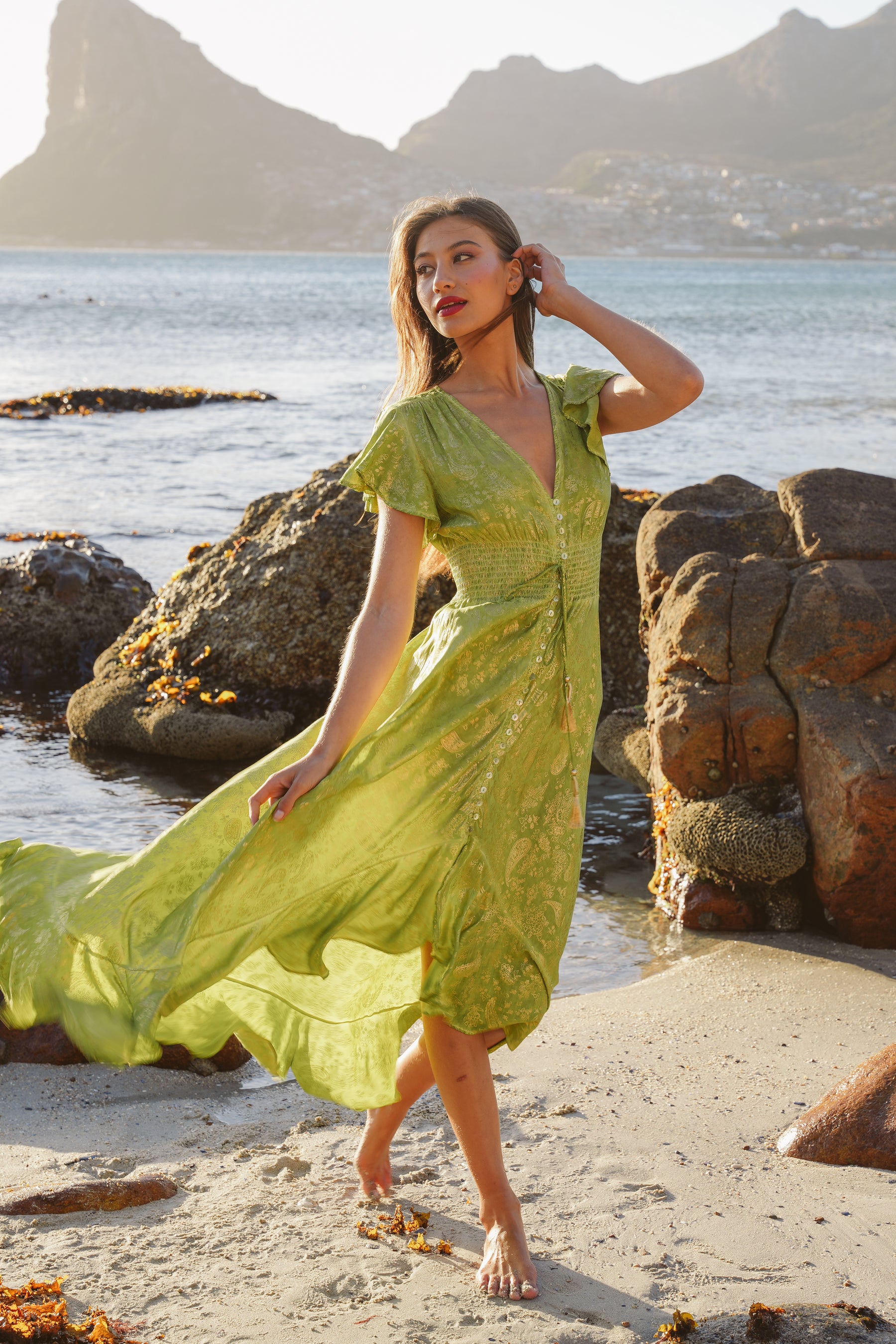 Woman in a green dress standing on a beach with mountains in the background