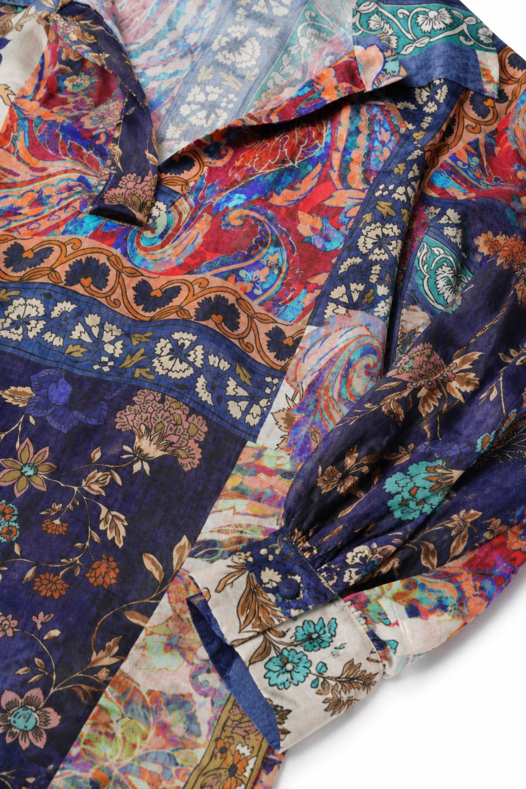 A close-up of a long-sleeve blouse with a highly detailed, multicolor paisley and floral print. The fabric features a mix of deep navy blue, red, orange, teal, and cream patterns.