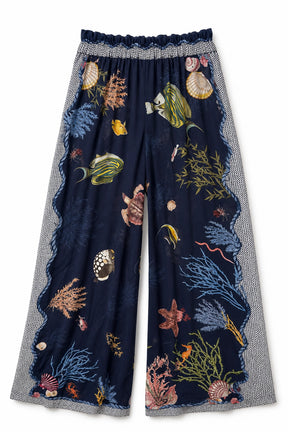 A pair of wide-leg pants featuring a dark navy blue base with an all-over underwater print of fish, starfish, coral, and seashells, finished with a gray and white patterned scalloped border.
