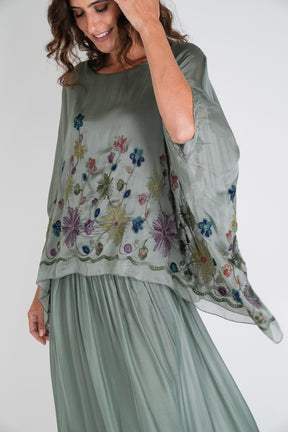 Woman wearing a light green top with floral embroidery on a white background