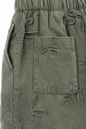 Close-up of olive green pants featuring a textured, raised leaf pattern and a front patch pocket.
