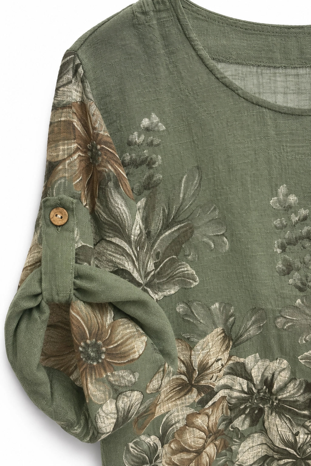 Close-up of an olive green top with a large floral print in muted brown, beige, and gray tones. The fabric has a textured, linen-like quality, and the sleeve is rolled up to show a small wooden button.