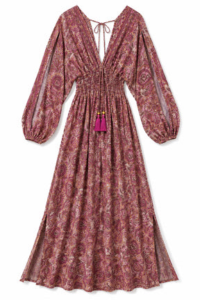 A long-sleeved midi dress with a dusty rose and beige paisley pattern, featuring a deep V-neckline with a tie, a smocked waist, and a bright magenta tassel accent.