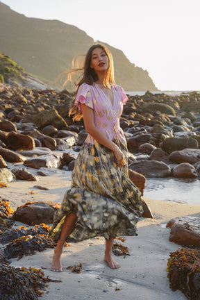 Woman in a colorful dress standing on a rocky beach with mountains in the background