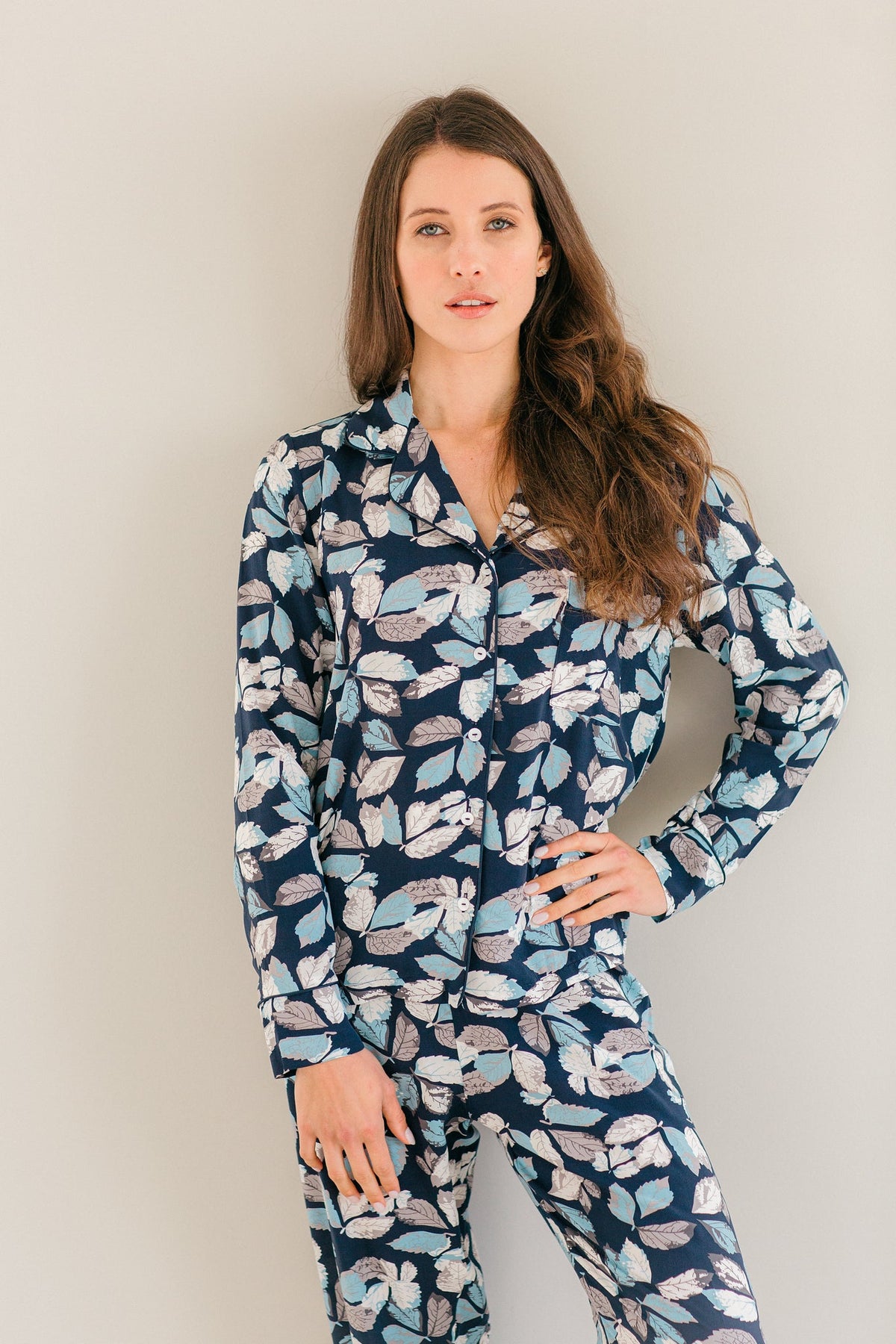 A woman modeling a matching long-sleeve pajama set with a navy blue base and a light blue, white, and pink floral pattern, set against a plain light gray background.