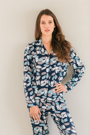 A woman modeling a matching long-sleeve pajama set with a navy blue base and a light blue, white, and pink floral pattern, set against a plain light gray background.