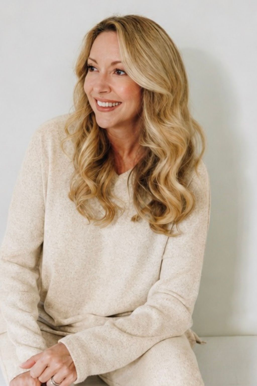 Woman with long blonde hair wearing a beige sweater against a plain background