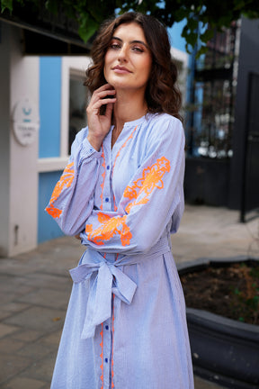 Woman wearing a light blue dress with orange floral embroidery outdoors.