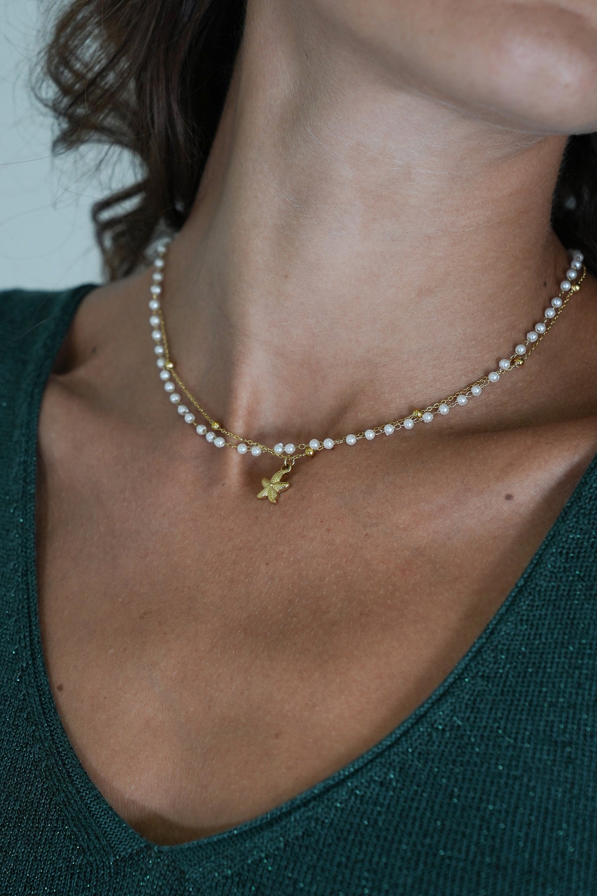 Pearl necklace with a gold star pendant worn by a person in a green top.