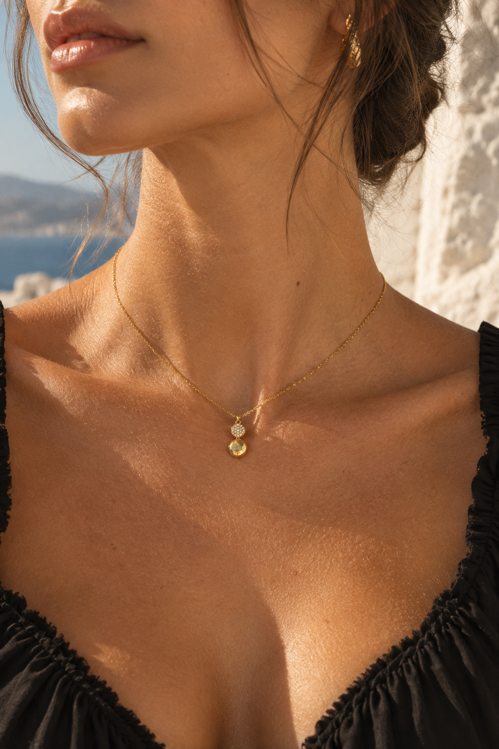 A close-up lifestyle shot of a woman wearing a delicate gold chain necklace with a small double-circle pendant, set against a bright outdoor background.
