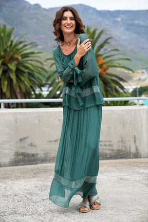 Woman in a teal dress standing outdoors with mountains and palm trees in the background