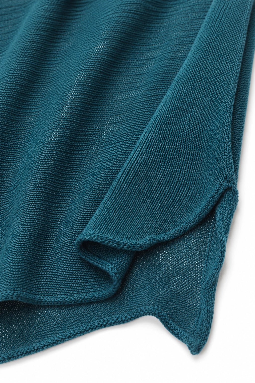 Close-up of a teal blue-green knit fabric with a fine ribbed texture and draped folds, shown against a white background.